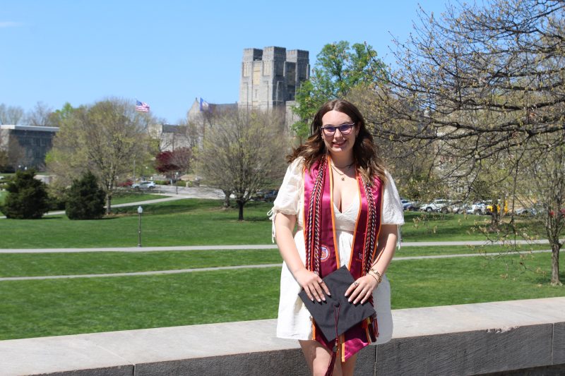 Emily Gannon standing in regalia by the Virginia Tech Pylons with Burruss Hall in the background.
